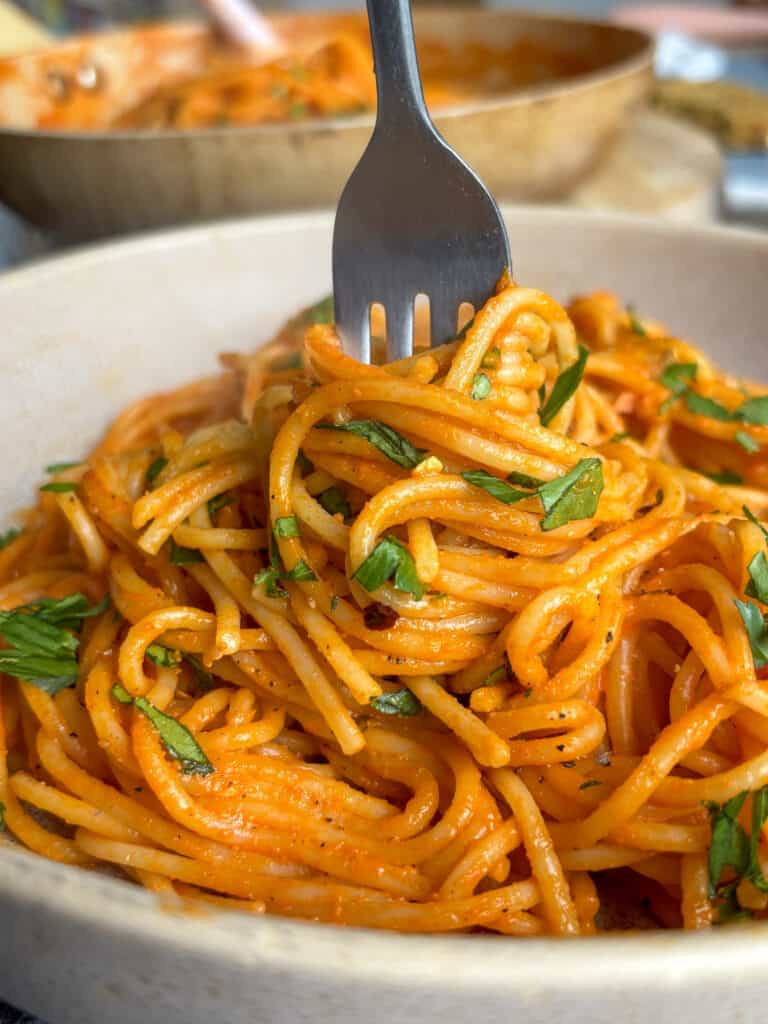 a close up shot of roasted red pepper pasta in a bowl, a fork twirling a large portion of it