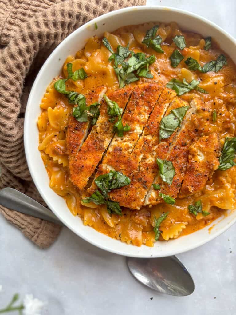 an overhead shot of the marry me pasta topped with the slice crispy tofu and chopped fresh basil, all served in a white bowl