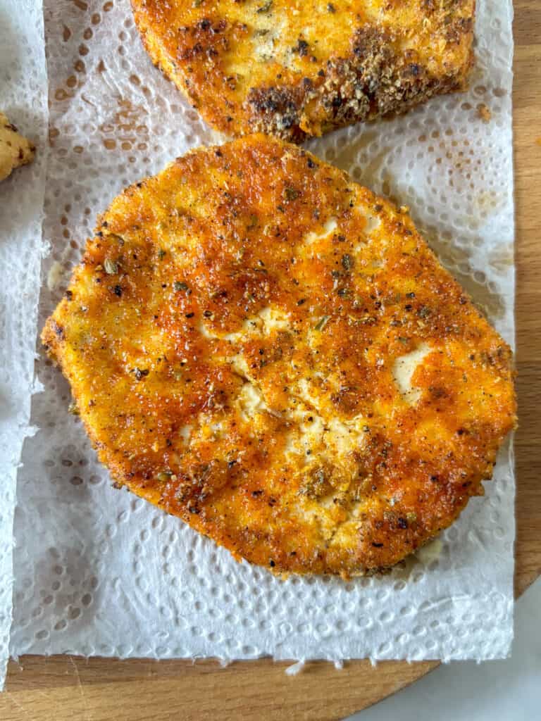 a slice of tofu coated in cornflour and spicy seaosnings and fried. The tofu is on a piece of kitchen roll to soak up any exces oil
