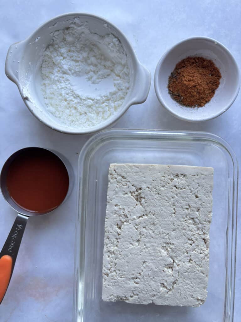 overhead shot of the ingredients to make buffalo tofu for these wraps. Tofu, buffalo, sauce, cornflour, and a seasoning blend of smoked paprika, oregano, cayenne pepper, garlic powder, and salt & pepper.
