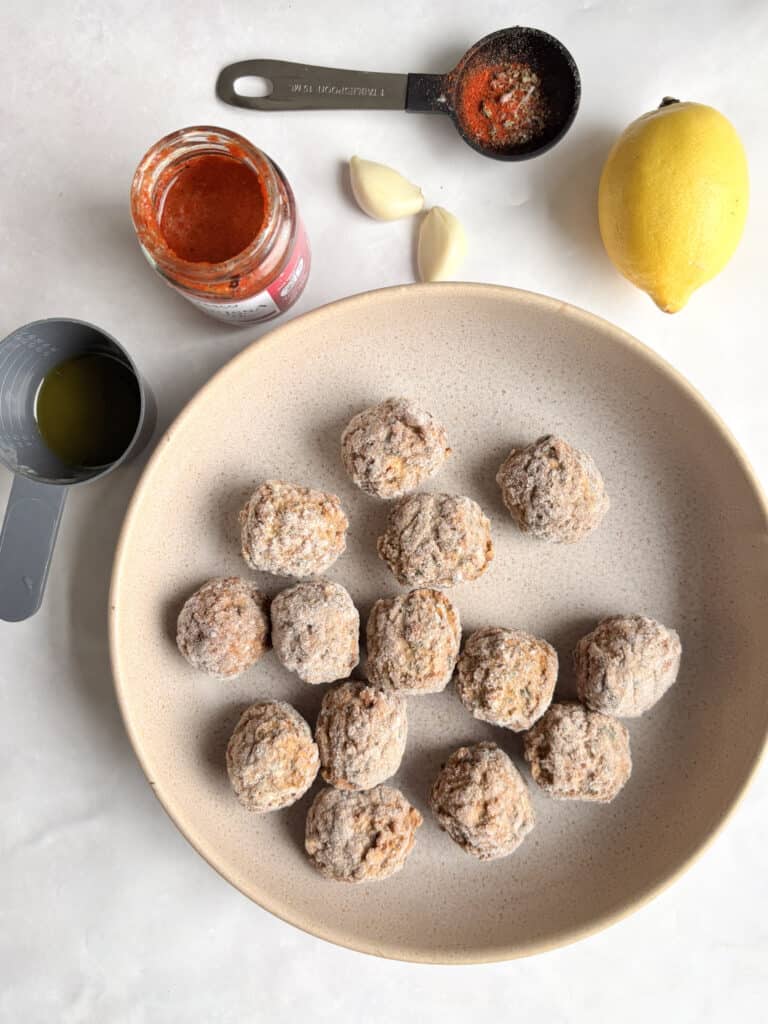the ingredients list for these harissa meatballs: frozen vegetarian meatballs, olive oil, harissa paste, garlic, smoked paprika, oregano, and lemon.