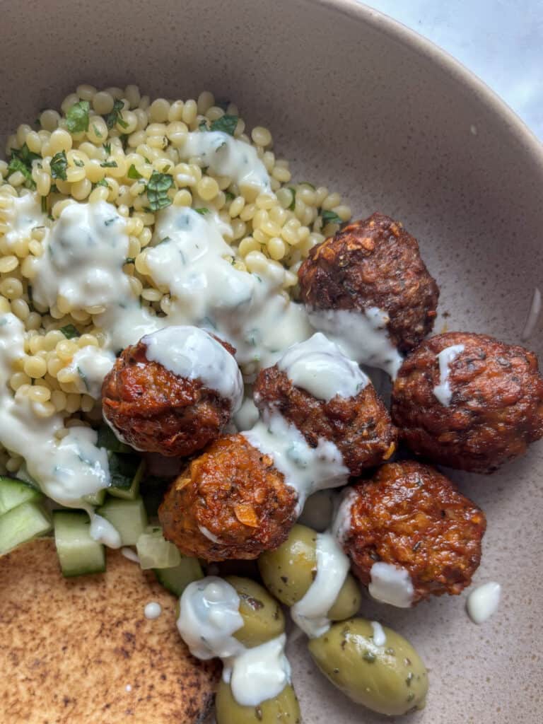 a close up shot of the harissa meatballs and peal couscous drizzled with the whipped feta yogurt dressing.