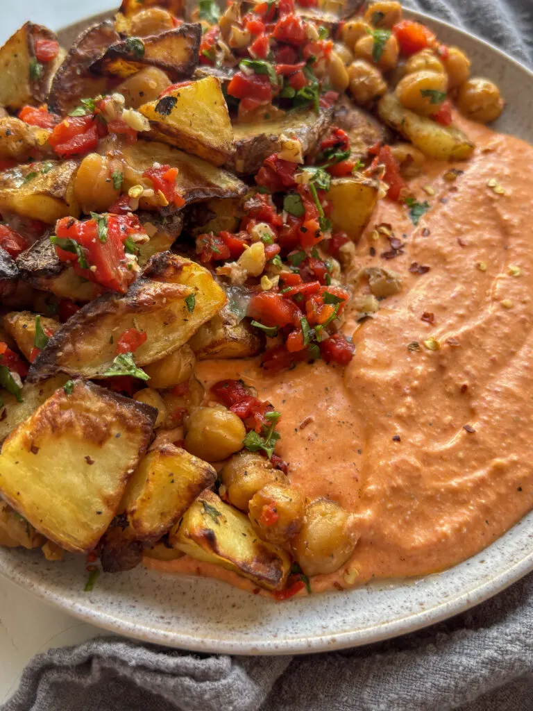 a close up shot of the red pepper feta dip, half of it topped with a medley of roast potatoes and chickpeas dressed in red pepper, walnuts, and parsley