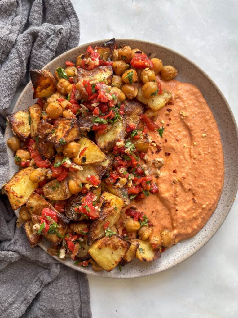 an overhead shot of the roasted red pepper feta dip, with half the plate topped with roasted potatoes and crispy chickpeas dressing with red peppers, walnuts, and parsley.