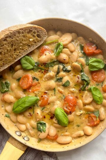 overhead shot of a pan of creamy butter beams topped with basil and a slice of crusty bread on the side