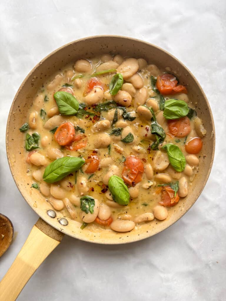 a saucepan of creamy butter beans topped with chili oil and fresh basil
