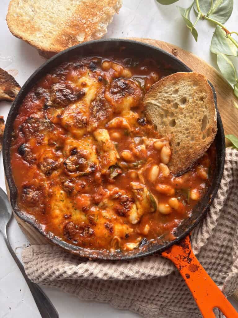 a cast iron skillet with cheesy white beans in a tomato sauce. Served with sour dough on the side.