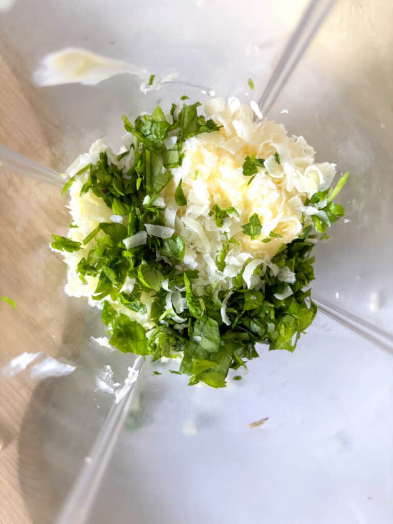 all the ingredients you'll need for the homemade garlic butter placed in the blender: butter, parsley, pecorino, garlic