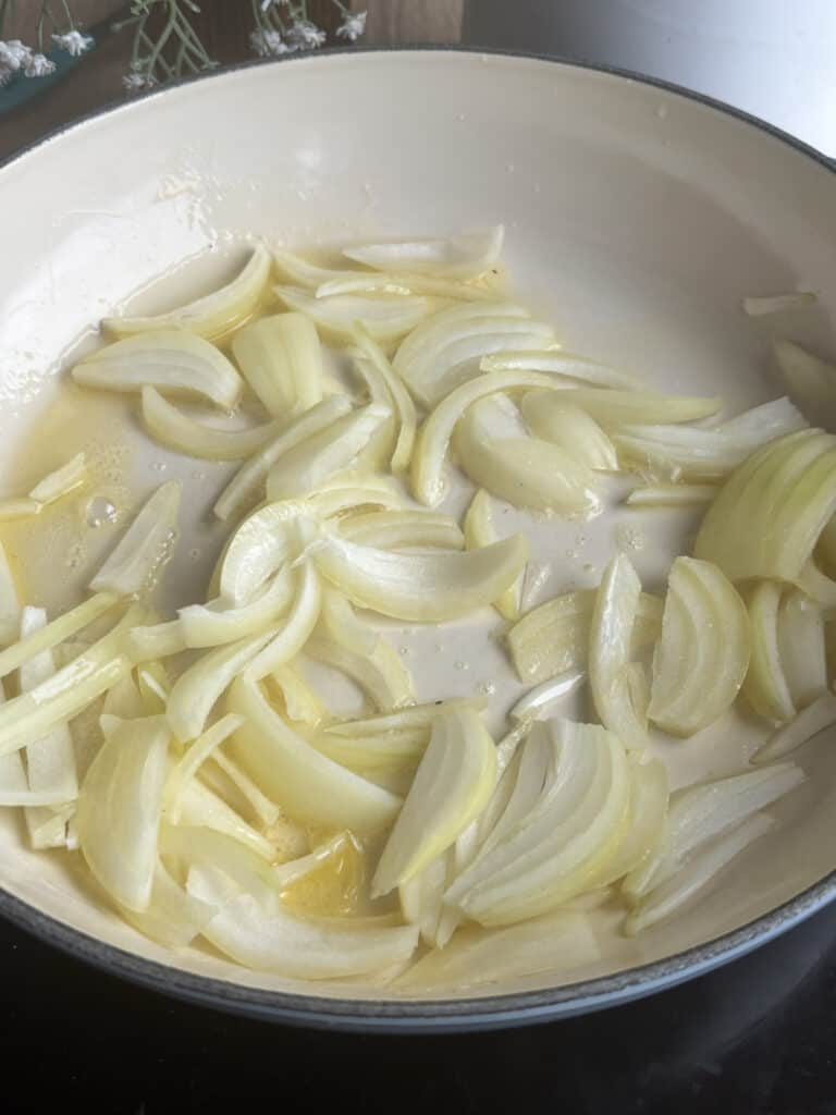sliced white onion is cooked in melted butter in a white pan