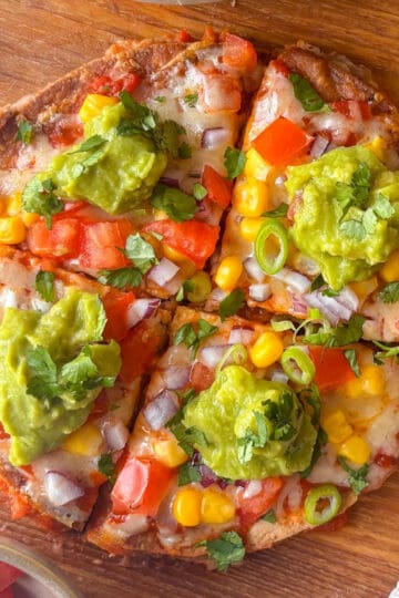 Mexican pizza on a chopping board, each quarter topped with guacamole