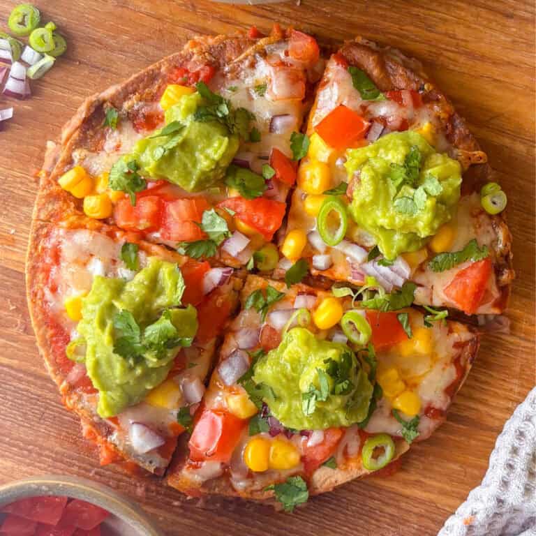 Mexican pizza on a chopping board, each quarter topped with guacamole