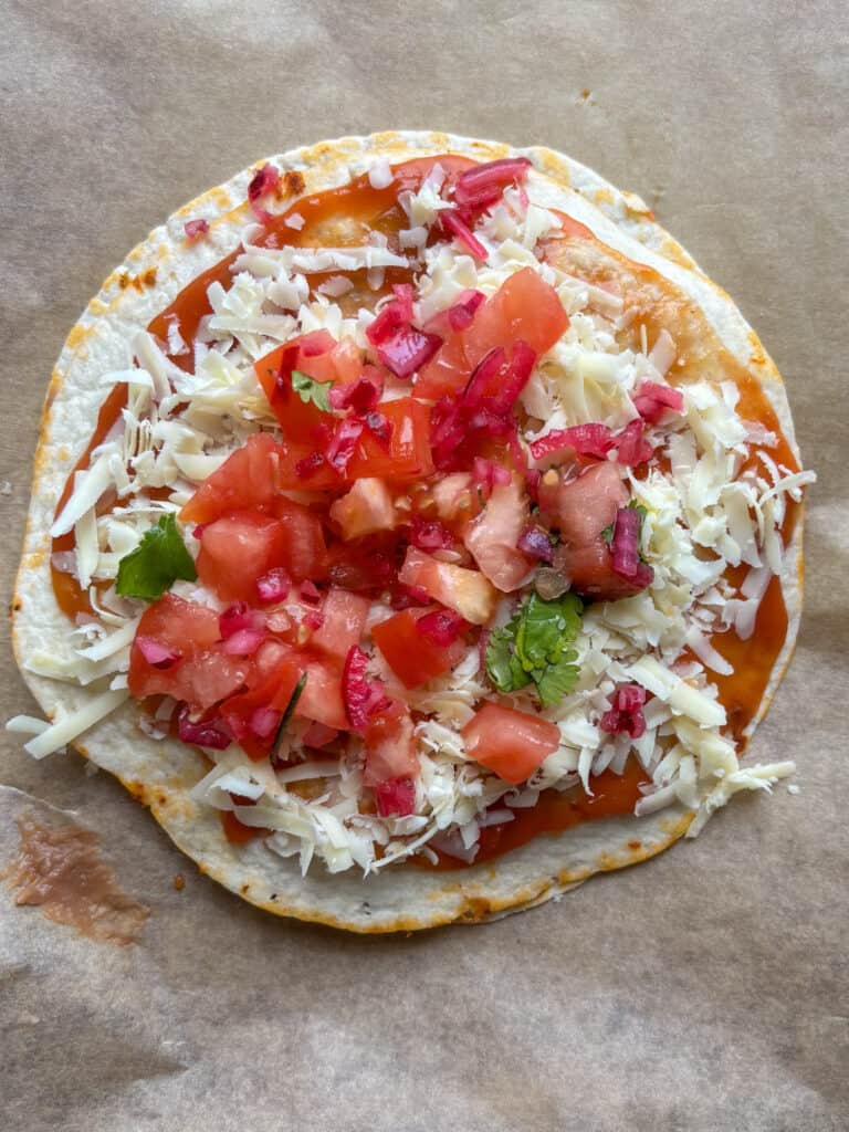 Uncooked Mexican pizza topped with sauce, cheese, and diced tomatoes