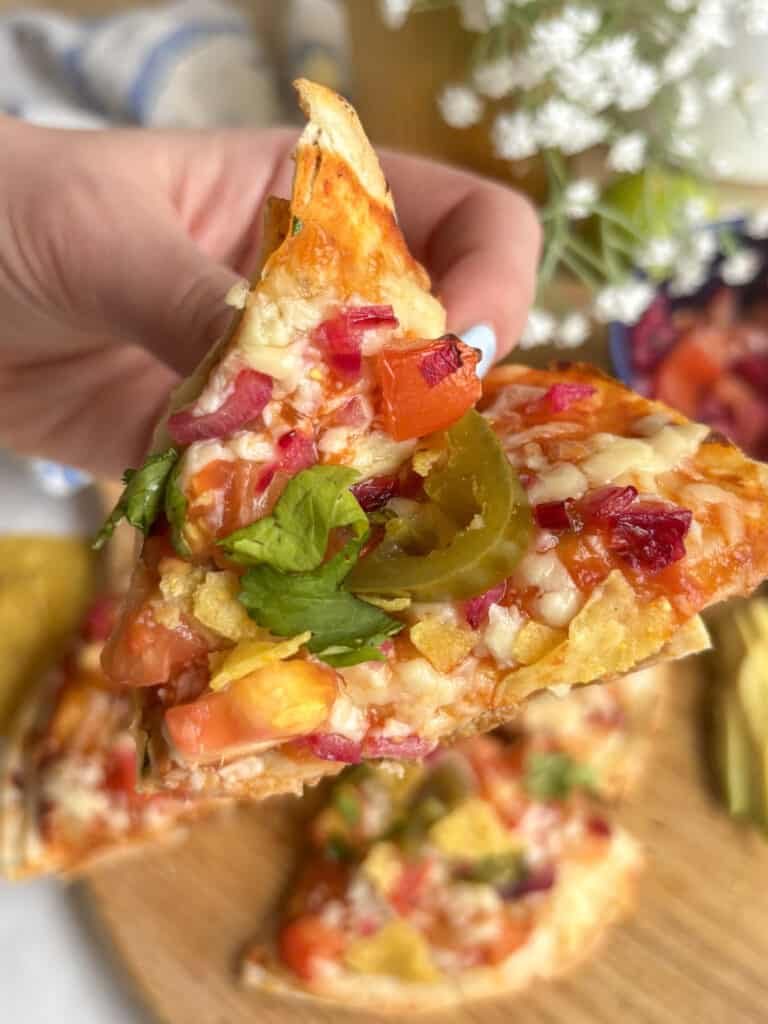 slice of Mexican pizza topped with pico de gallo, crushed nacho chips, and jalapeno