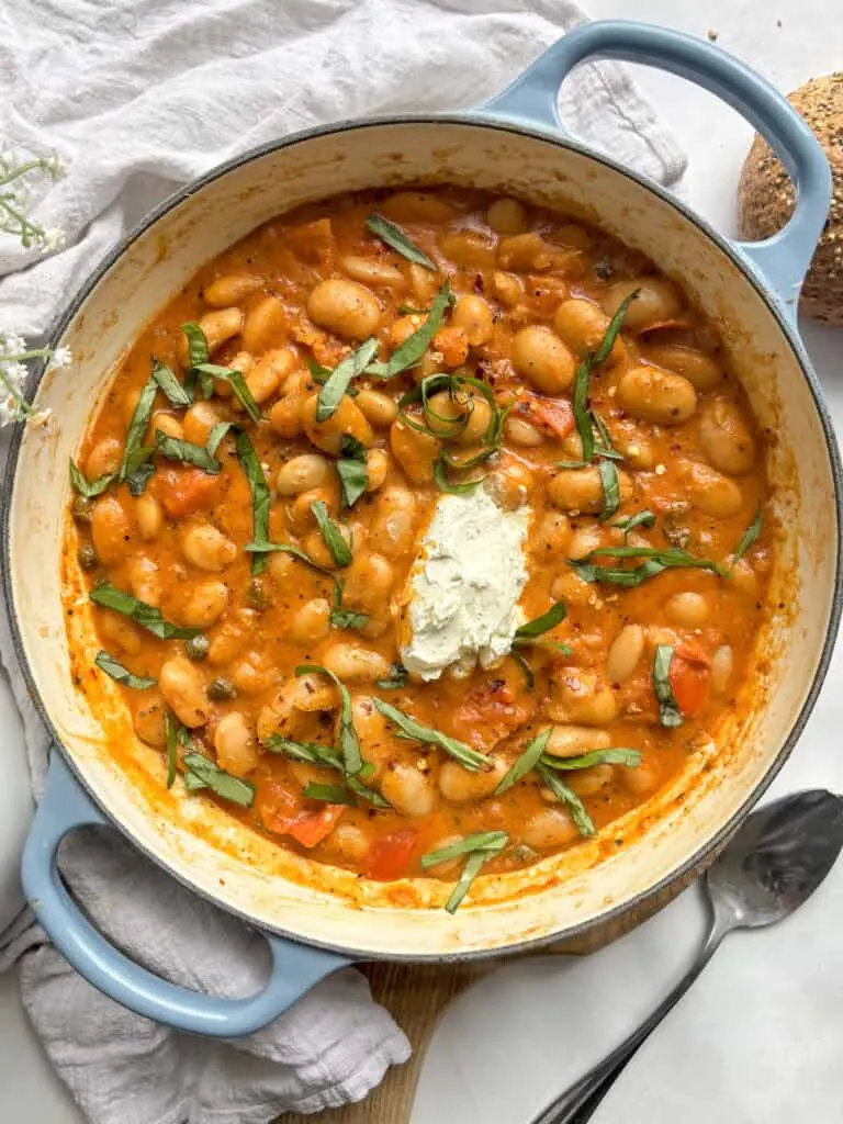 a casserole dish of red pesto butter beans topped with garlic & herb cream cheese and fresh basil