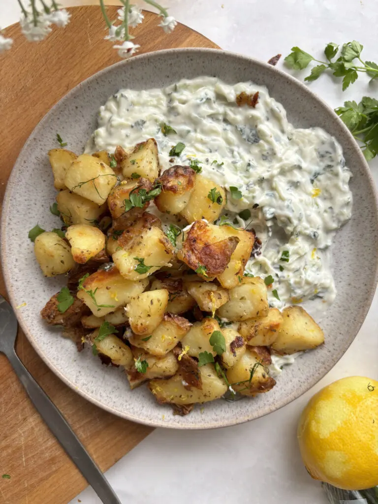 a plate of crispy dill roasted potatoes with lemon zest, served on top of tzatziki cucumber dip