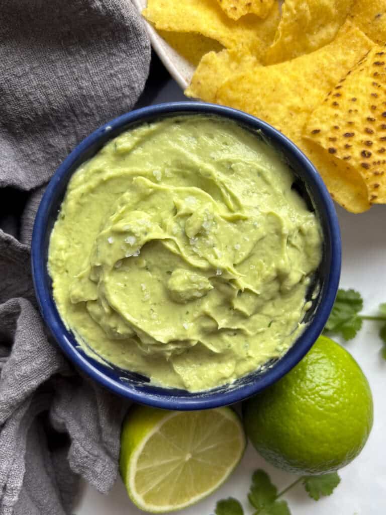 avocado lime crema served in a blue bowl with tortilla chips off to the side