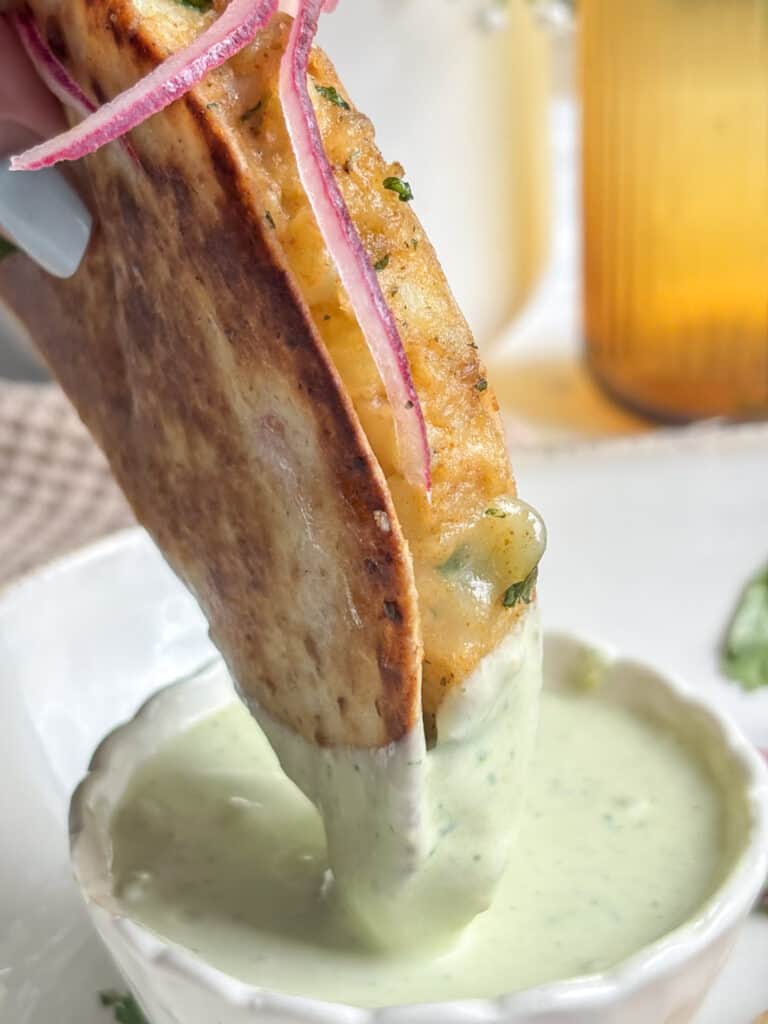 a close up shot of a crispy potato taco being dipped in a creamy jalapeno dip