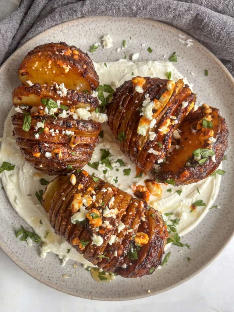 overhead shot of cooked harissa hasselback potatoes sprinkled with feta and on a bed of tahini yogurt dressing.