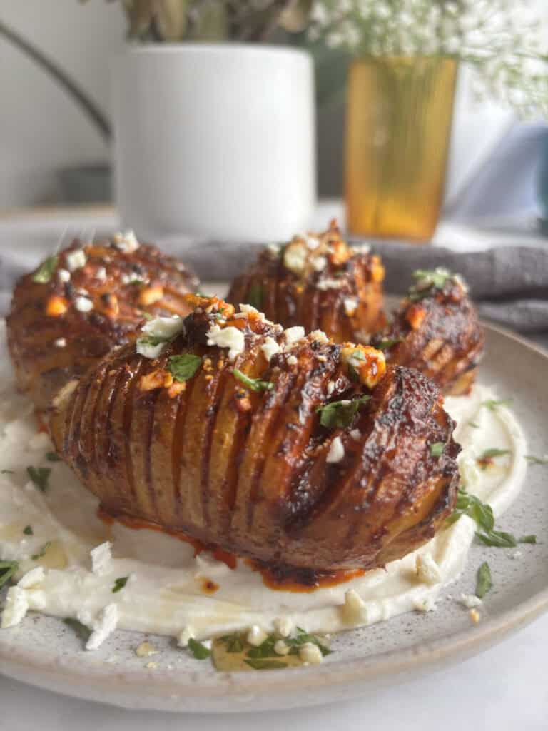 cooked harissa hasselback potatoes close up shot served on a yogurt sauce and sprinkled with feta