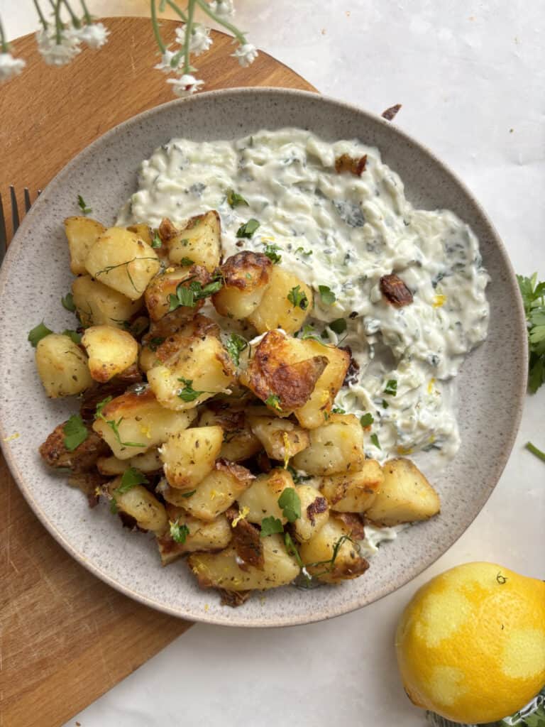 crispy lemon and thyme potatoes on top of a plate of cooling tzatziki sauce (cucumber dip)