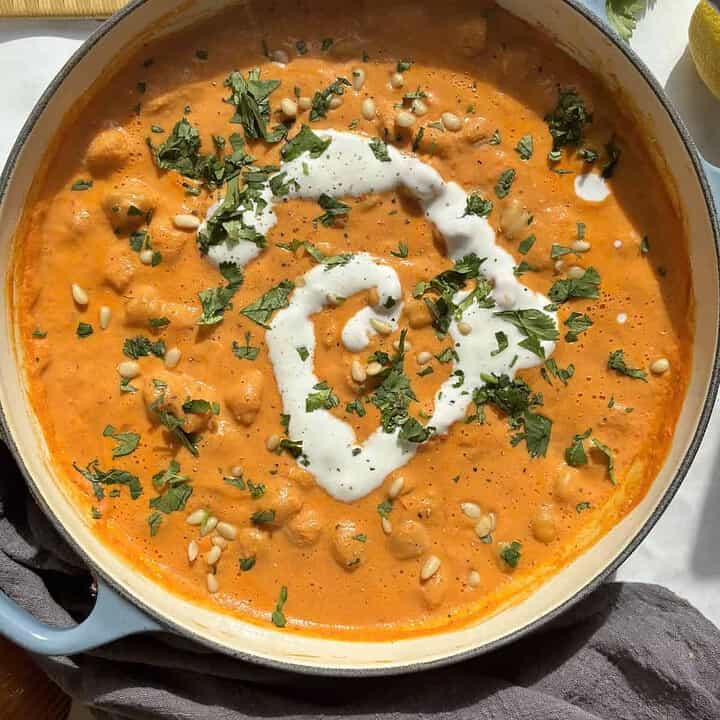 vegan romesco chickpeas in a shallow casserole dish with a cream of cream and chopped parsley