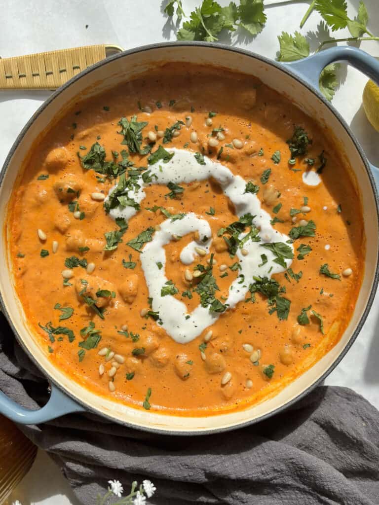 vegan romesco chickpeas in a shallow casserole dish with a cream of cream and chopped parsley