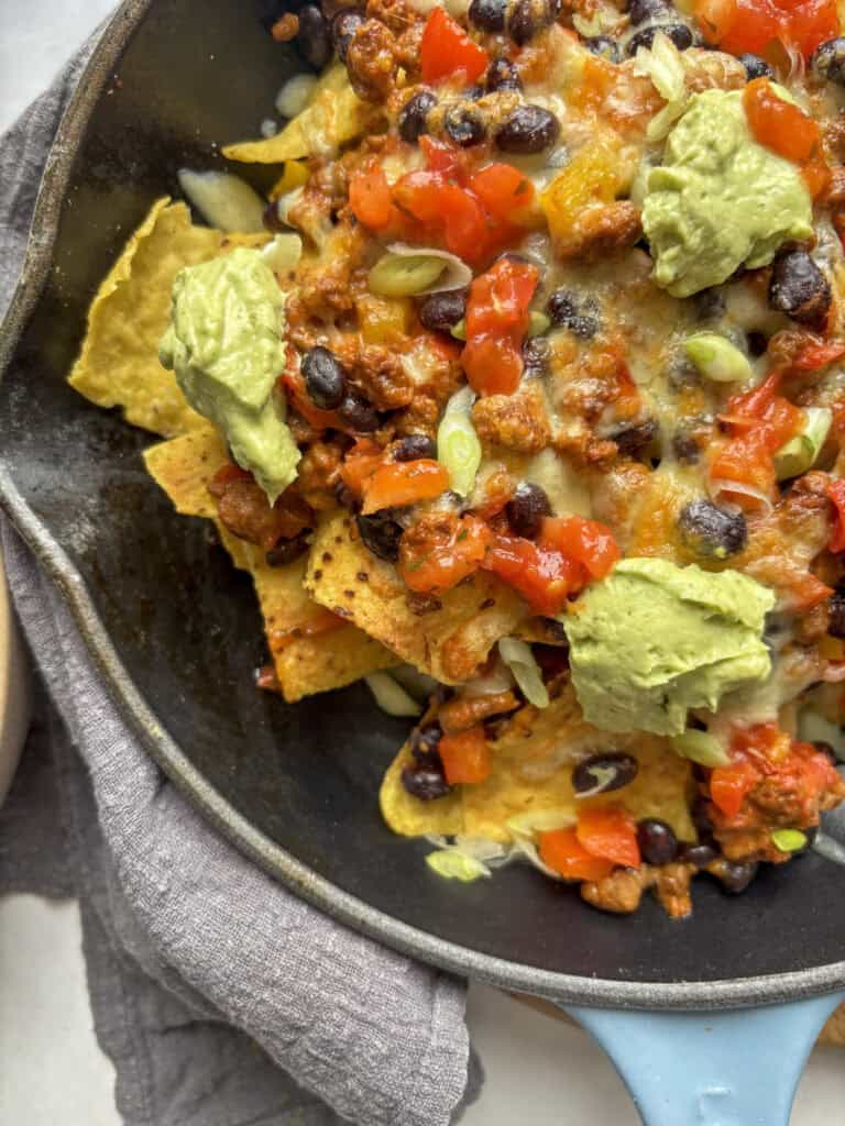 a close up shot of the finished skillet nachos, loaded with mince, black beans, avocado crema, fresh salsa, and melted cheese