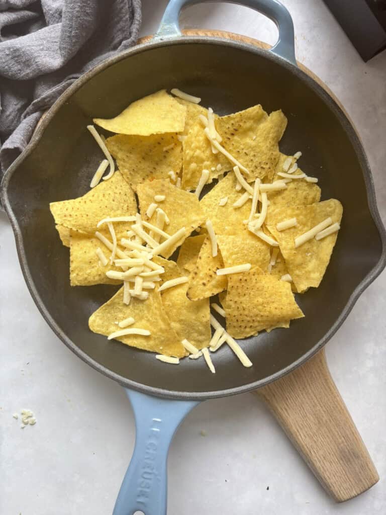 tortilla chips in a skillet topped with a small amount of grated cheese