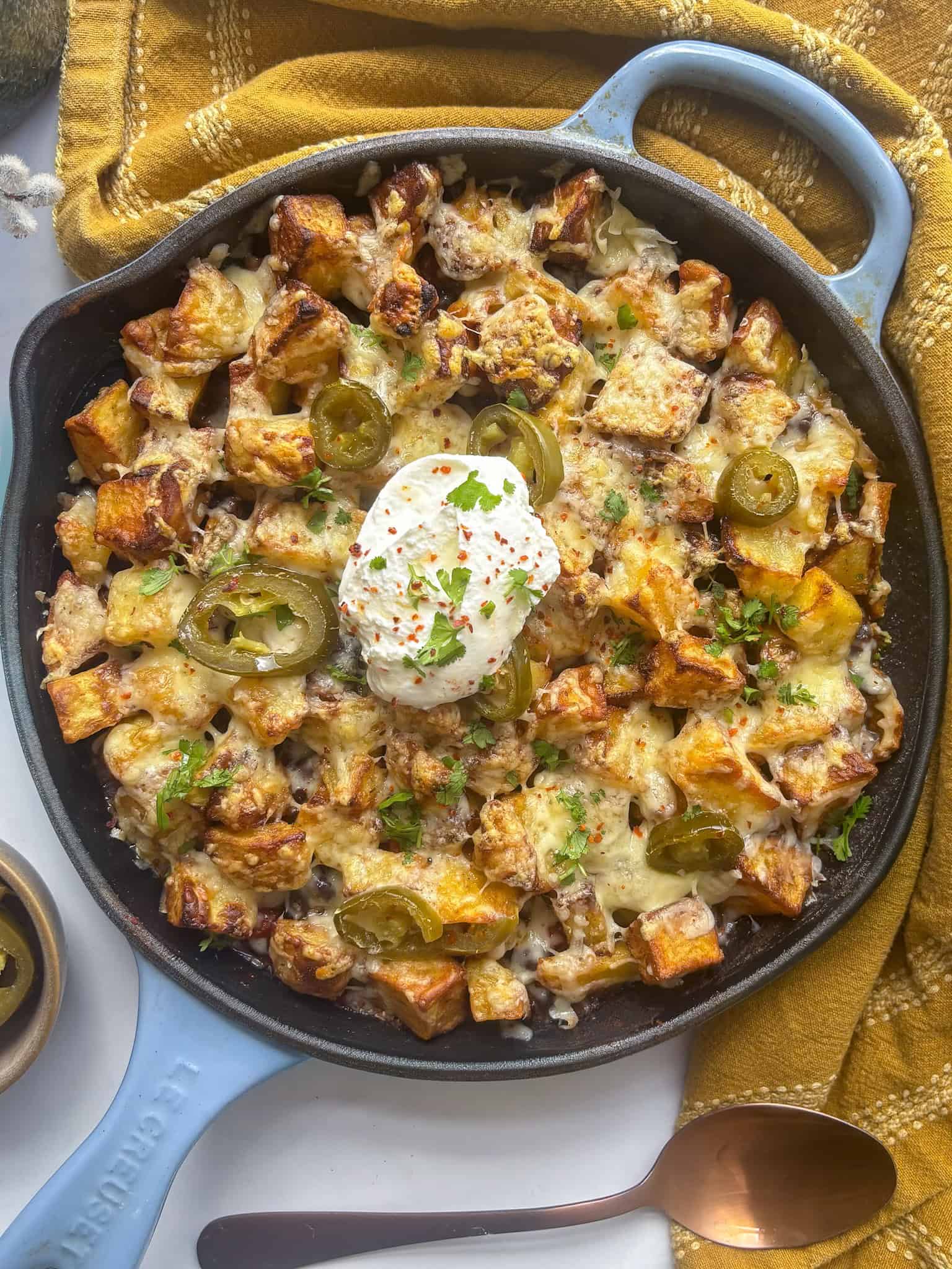 a cast iron skillet of smoky chipotle black beans topped with crispy cubed potatoes, melted cheese, and jalapenos, with a spoonful of yogurt on the top.