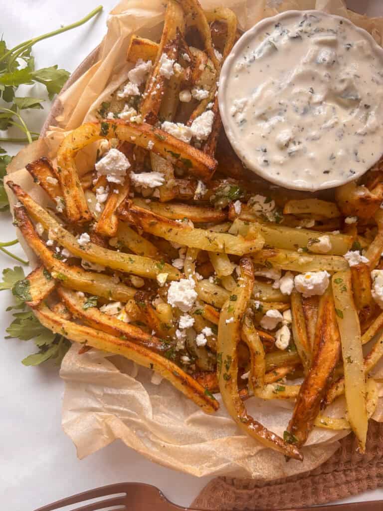 plate of Greek fries topped with crumbled feta and fresh herbs, with a dip of tzatziki next to it