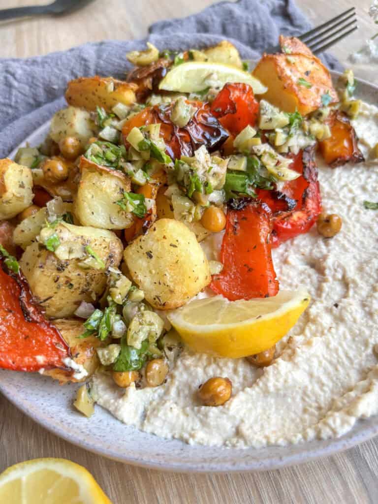 roasted potato, chickpea, and pepperswith olive salsa verde, served on top of a plate of creamy hummus