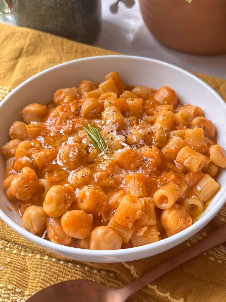 pasta e ceci in a white bowl topped with black pepper, hard cheese, and rosemary