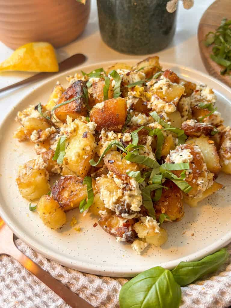 a side on view of baked feta potatoes with red chilli flakes and fresh basil