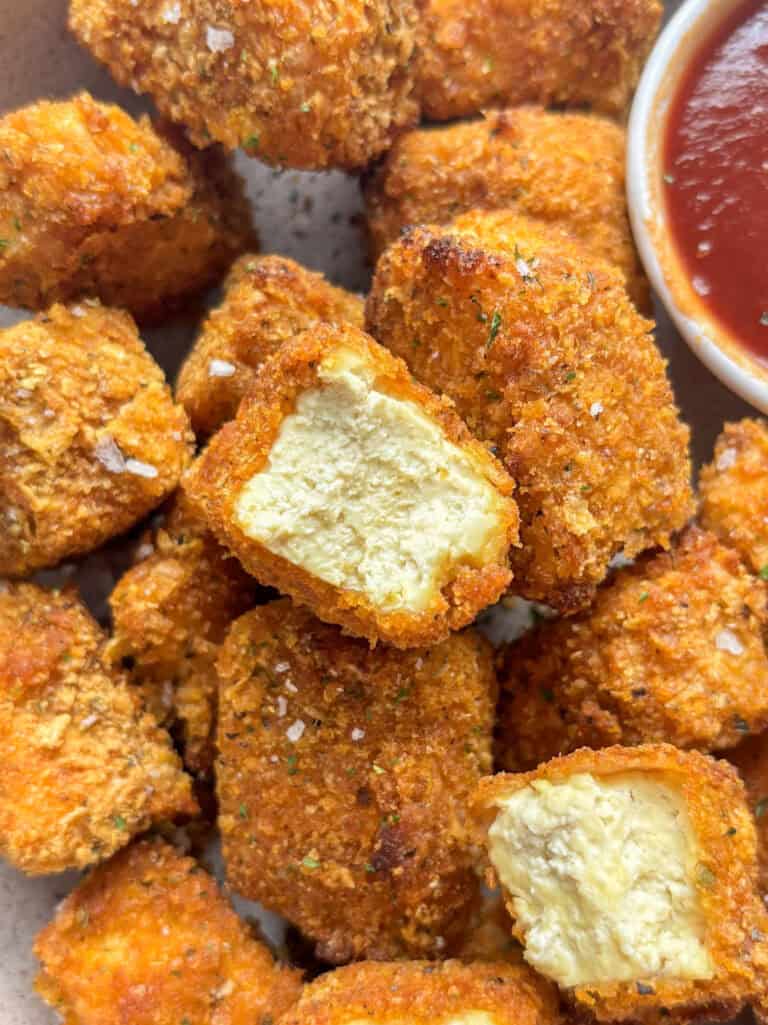a pile of baked tofu nuggets with a golden breadcrumb coating topped with flaky sea salt and herbs