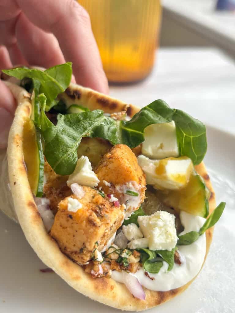 a vegetarian gyro wrap with sauce, salad, vegan chicken, and feta