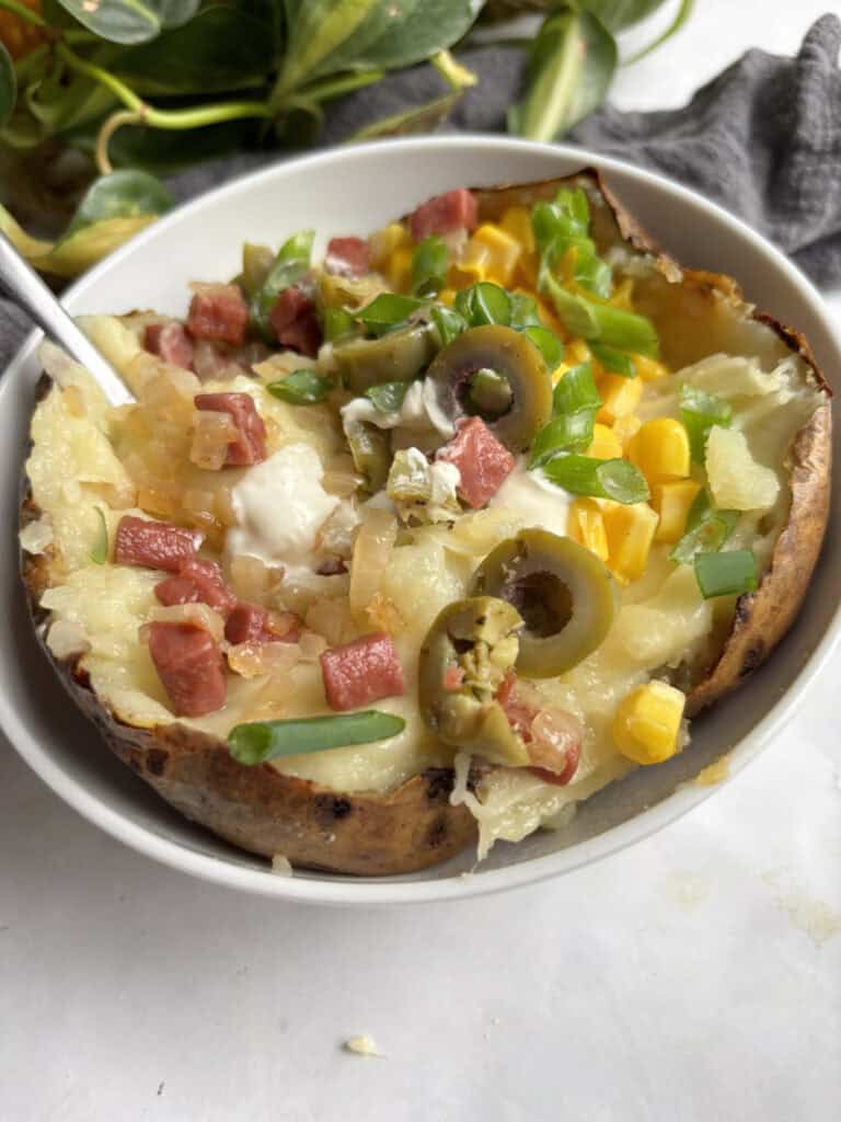 a bowl of kumpir (stuffed baked potato) loaded with sour cream, vegetarian bacon and onions, chopped olives, sweetcorn, and chives