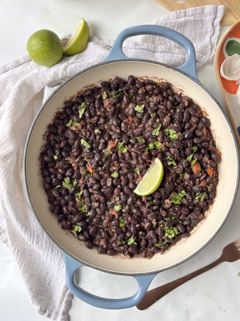 a casserole pan of Mexican black beans topped with fresh herbs and a wedge of lime