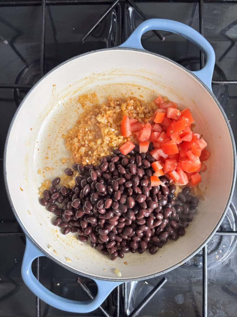 black beans and tomato added to a pan of diced onion, garlic, and seasonings for the Mexican black beans