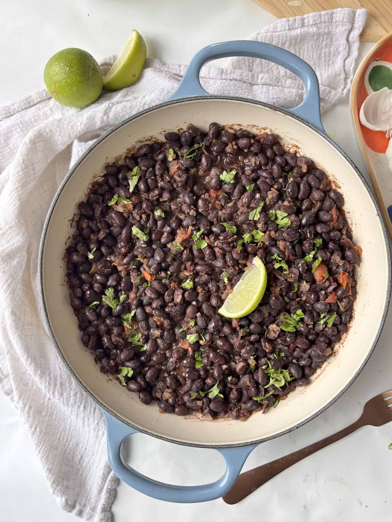 a casserole pan of Mexican black beans topped with fresh herbs and lime