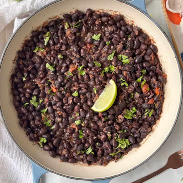 casserole pan of mexican black beans topped with fresh herbs and a lime wedge