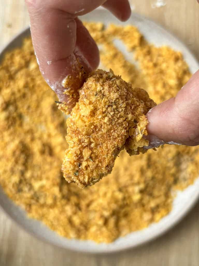 tofu being dipped in cornflake crumb & seasoning mixture