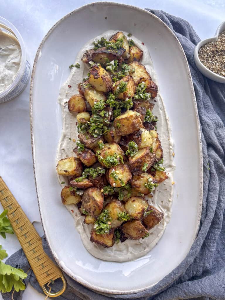 a large oval serving plate of za'atar potatoes on top of a creamy tahini dip
