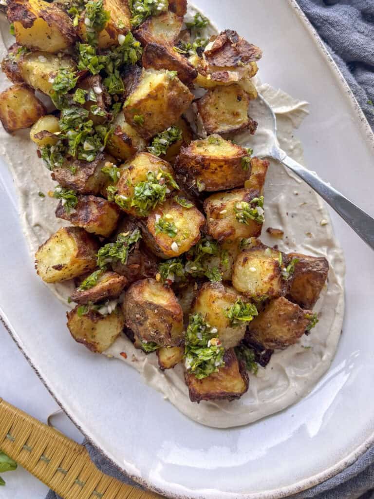 a serving plate of crispy za'atar potatoes on top of a bead of creamy tahini sauce
