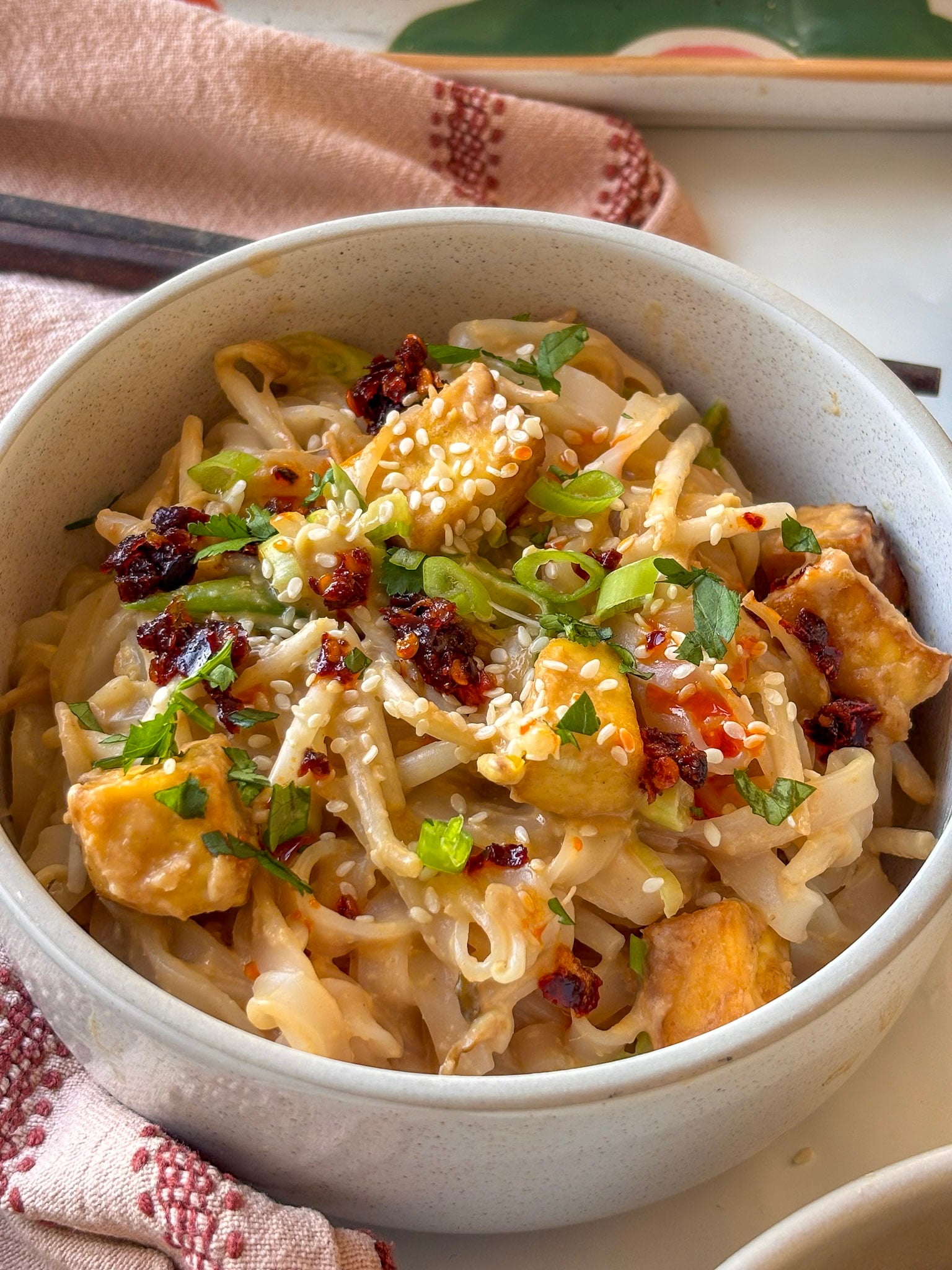 spicy peanut noodles with crispy tofu topped with sesame seeds and chilli crunch