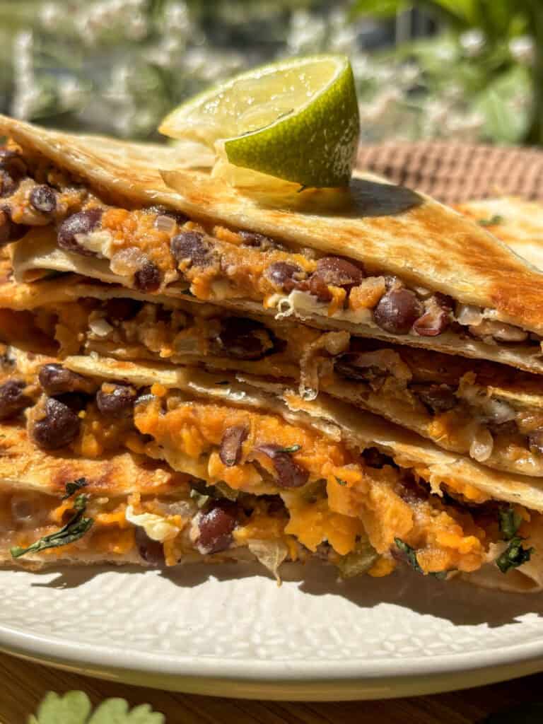a stack of sweet potato and black bean quesadillas on a white plate in the sunshine