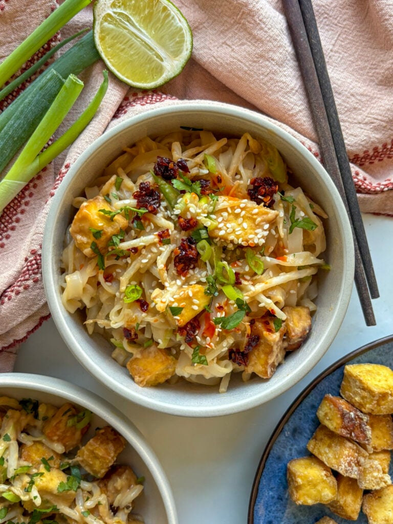 spicy peanut noodles with crispy tofu topped with sesame seeds and chilli crunch