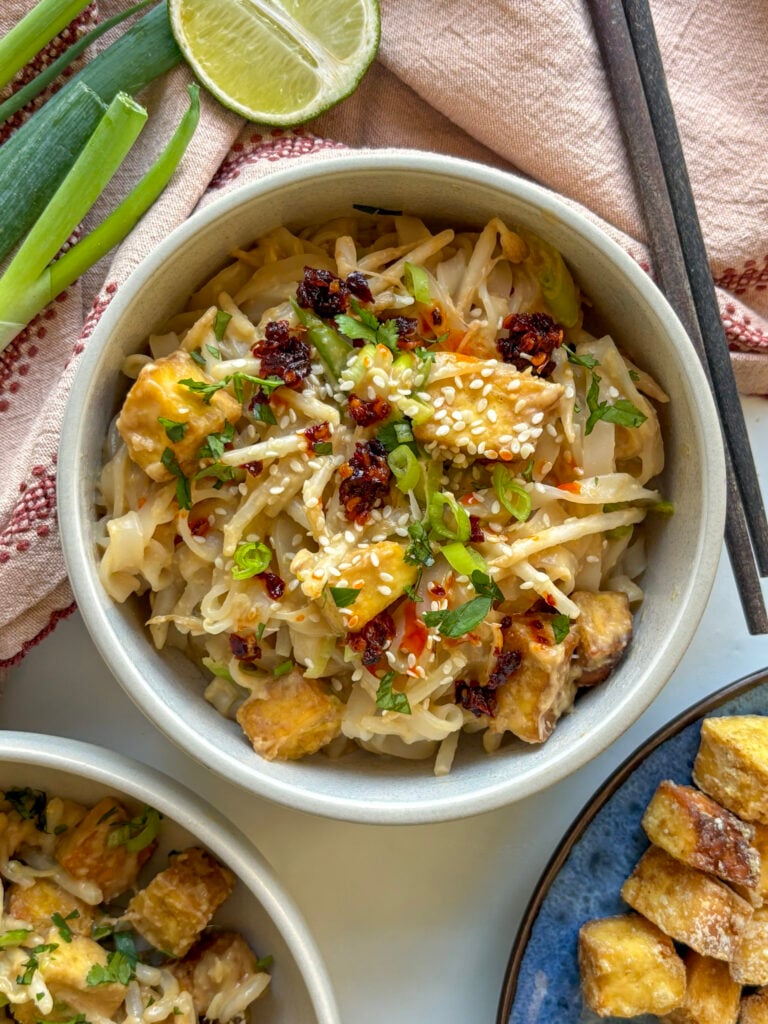 bowl of spicy peanut noodles with crispy tofu, topped with sesame seeds and chili crunch