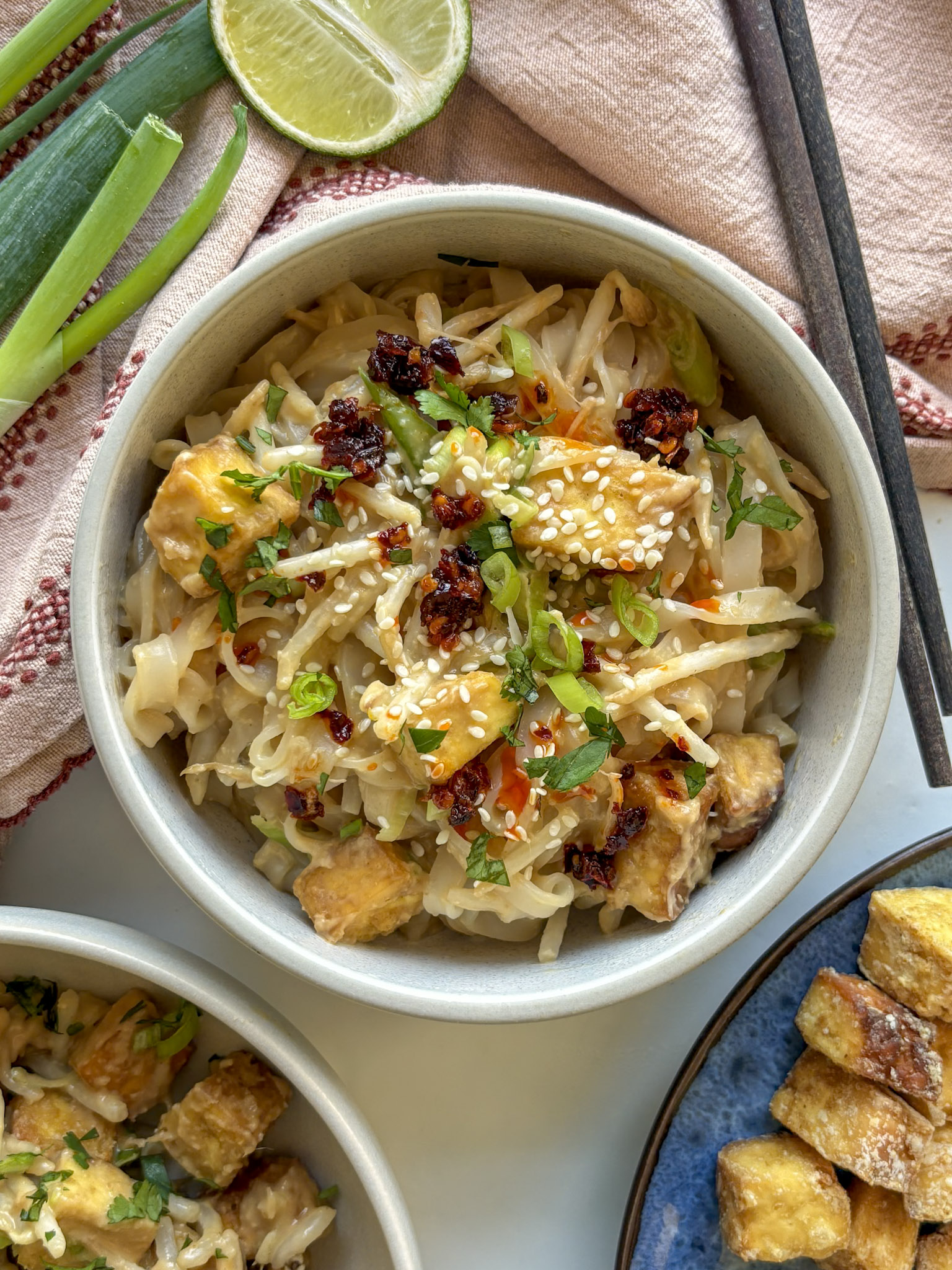 bowl of spicy peanut noodles with crispy tofu, topped with sesame seeds and chili crunch
