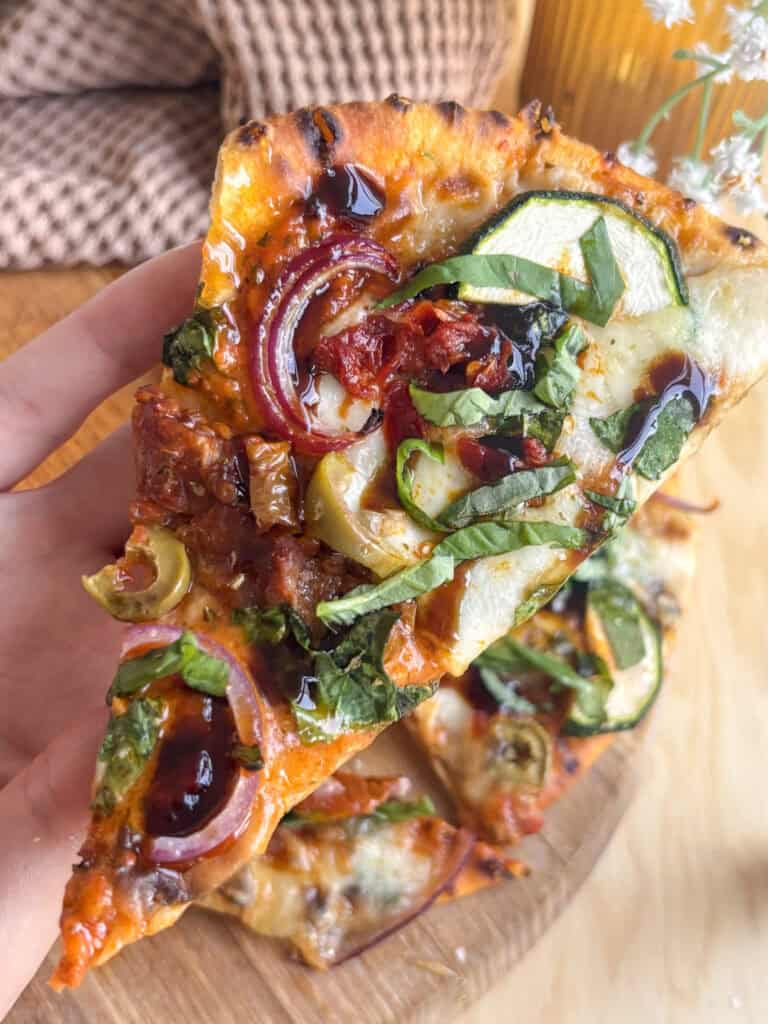 a slice of flatbread pizza topped with Mediterranean veegtables, mozzarella, balsamic glaze, and basil