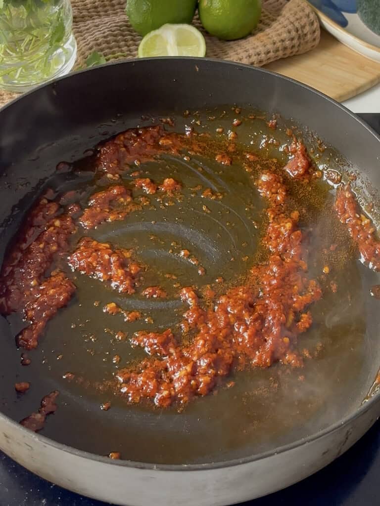 minced garlic, tomato paste, and chipotle paste being cooked in a saucepan